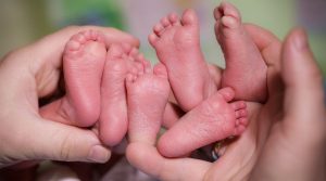 A mother is holding in the hands feet of newborn triplets baby.
